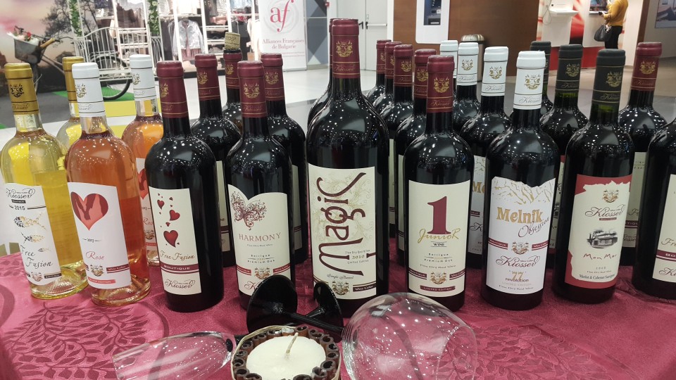 Бутилки червено вино, бяло вино и розе "Кьосев", наредени на маса по време на изложение